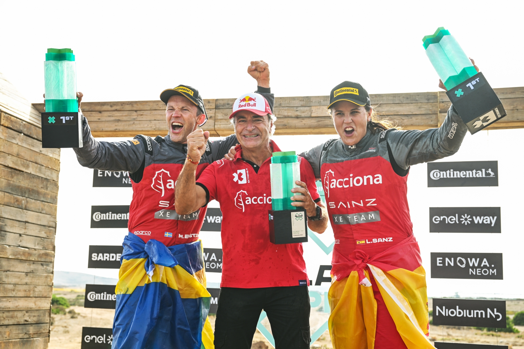 CAPO TEULADA, SARDINIA, ITALY - SEPTEMBER 16: Mattias Ekstrom (SWE), Acciona | Sainz XE Team, and Laia Sanz (ESP), Acciona | Sainz XE Team, 1st position, celebrate with Carlos Sainz (ESP), Acciona | Sainz XE Team, on the podium during the Island X-Prix II on September 16, 2023 in Capo Teulada, Sardinia, Italy. (Photo by Sam Bagnall / LAT Images)
